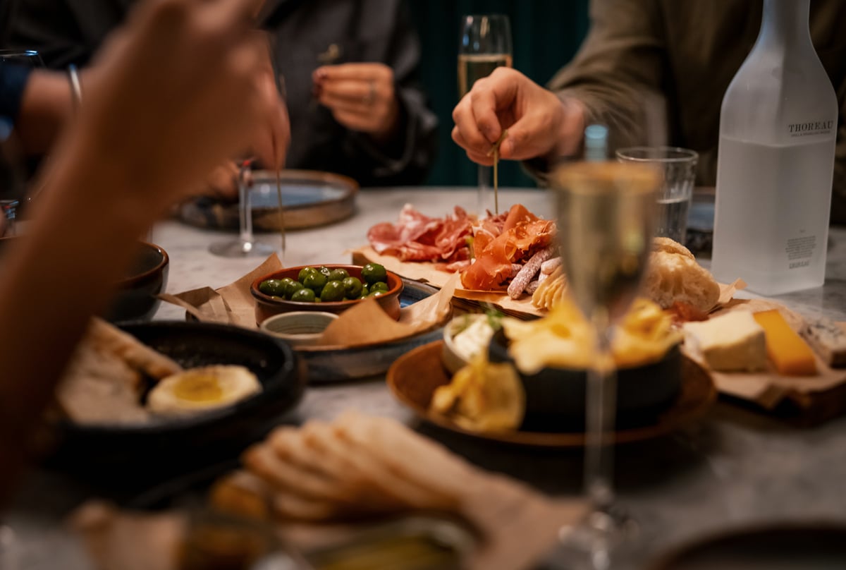 Personer som delar en charkbricka med ost, charkuterier och oliver, tillsammans med mousserande vin.